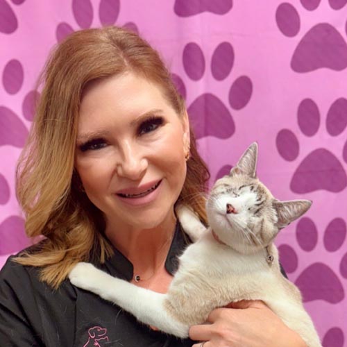 Woman smiling and holding a content cat with eyes closed against a pink background with paw prints.